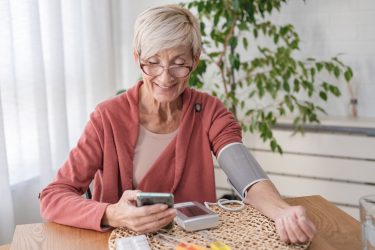 Older woman sitting alone at home, measuring her blood pressure with a home device